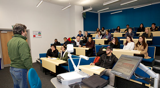 A male lecturer with a lecture theatre of students